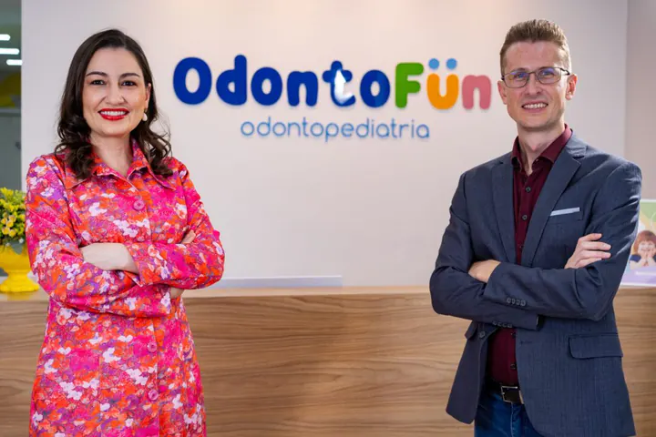 Dra. Bruna Meotti e Eduardo Meotti na recepção da Odonto Fun, com o logotipo da clínica ao fundo