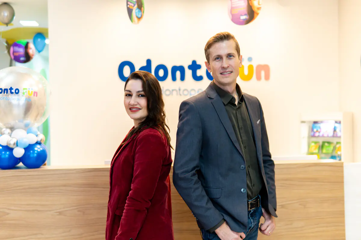 Dra. Bruna Meotti e Eduardo Meotti na recepção da Odonto Fun, com o logotipo da clínica ao fundo